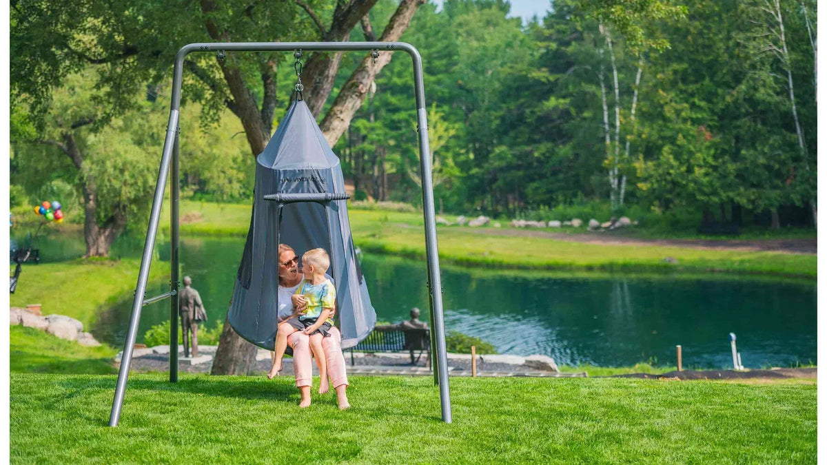 A mother and child sitting in a tent swing on a swing set.